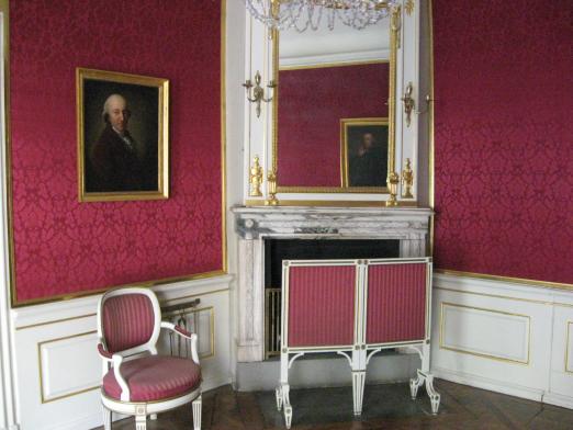 Einblick in den zweiten Roten Salon: Kamin, Spiegel und zwei der Portraits