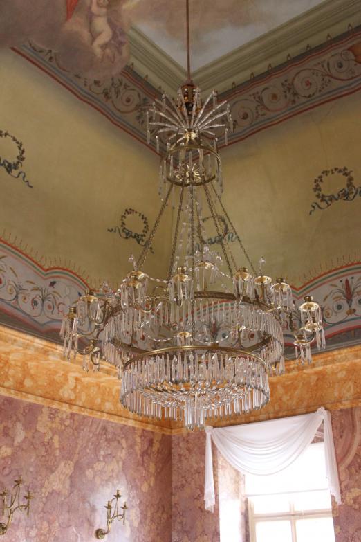 Auf dem Bild kann man einen Kronleuchter sehen, der im Festsaal hängt, ebenso die großen Fenster mit weißen Gardinen.